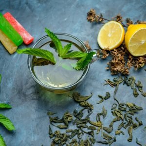 Tea in a cup with mint, dried herbs, lemon, sweeties flat lay on a dark blue background
